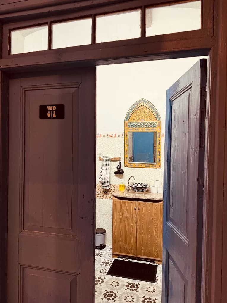 Surf camp WC Essaouira open lilac wooden double doors transom window vessel sink arched painted mirror geometric floor tiles