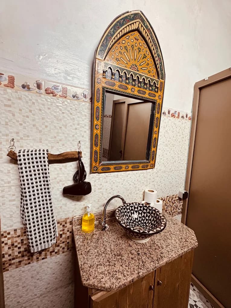 Surf camp bathroom Essaouira hand-painted Moorish arch mirror patterned vessel sink granite counter driftwood towel rack