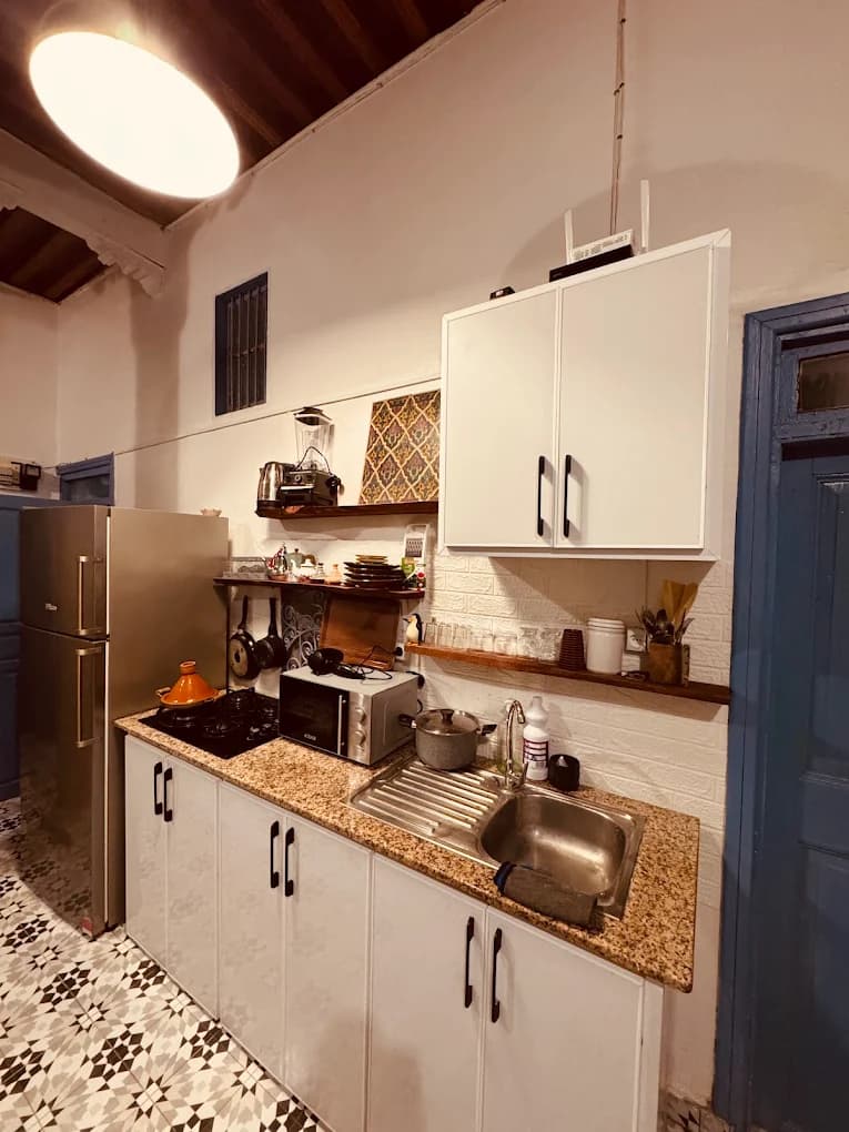 Surf camp communal kitchen Essaouira white cabinets granite counter tagine on stove blue doorframe patterned Moroccan tiles WiFi