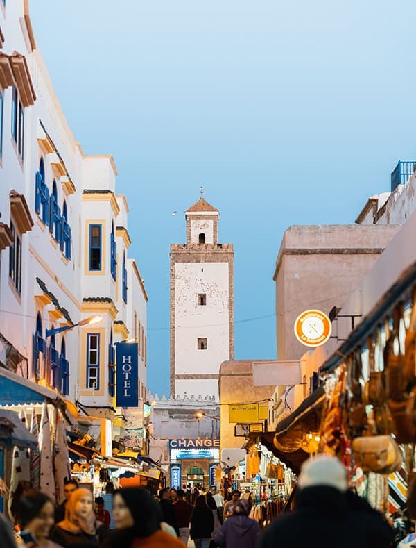 Busy Essaouira medina street with minaret, shops, and blue-trimmed buildings near surf camp Essaouira Morocco