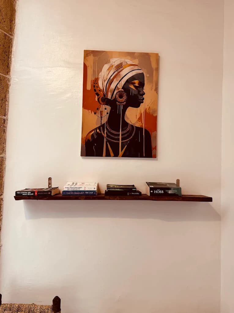 Surf camp Essaouira lounge wall portrait painting wooden guest bookshelf paperbacks English French wicker chair stone pillar