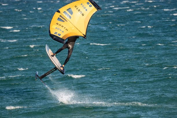 Wingfoiler airborne above the Atlantic off Essaouira — yellow wing, foil board clear of the water
