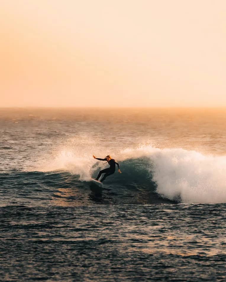 Solo surfer in black wetsuit riding an Atlantic wave at golden hour — Essaouira Morocco surf school hero