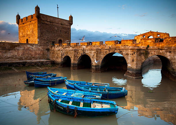 Essaouira Skala fortress and blue fishing boats in the port at golden hour, Morocco