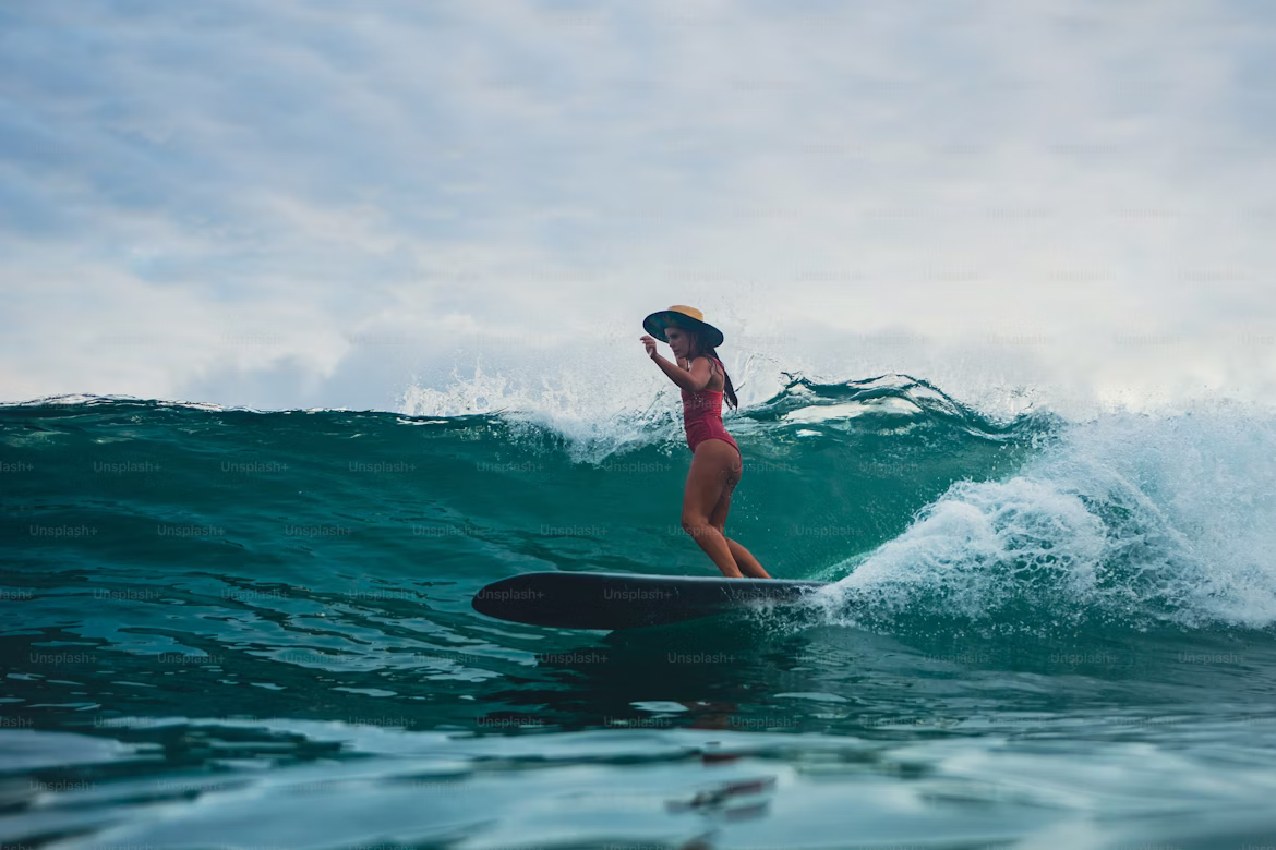 Surfer in a red swimsuit and straw hat riding a turquoise Atlantic wave — beginner surf Essaouira Morocco