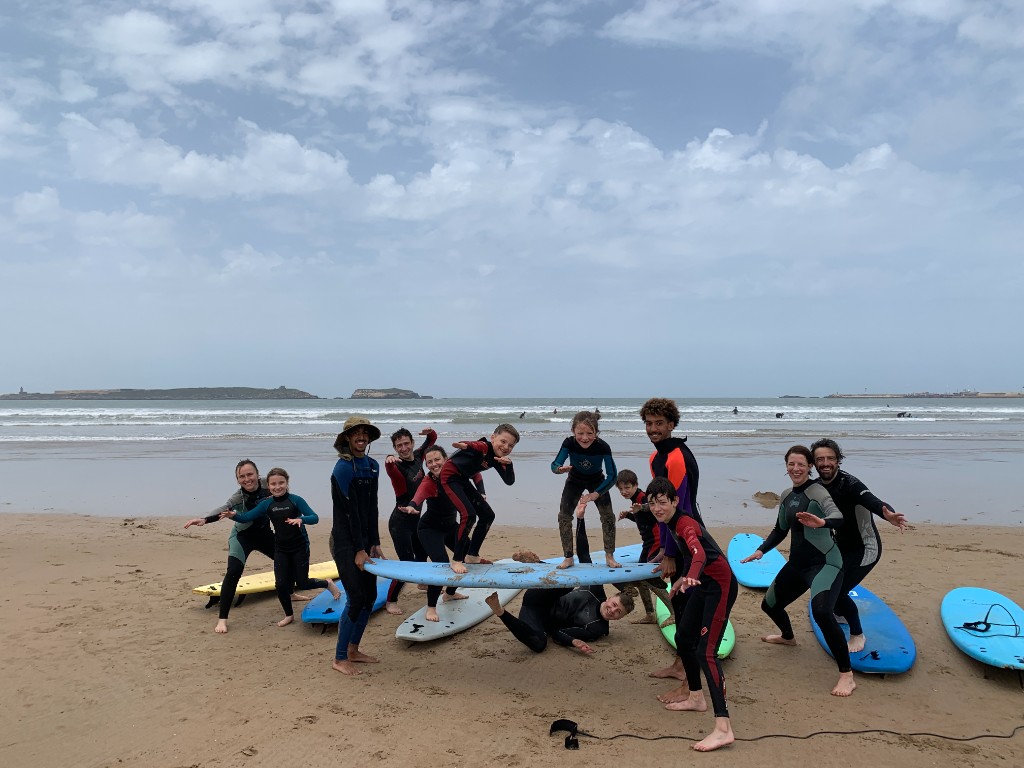 Surf students and coaches in wetsuits with boards on Essaouira beach — group lesson, Atlantic bay